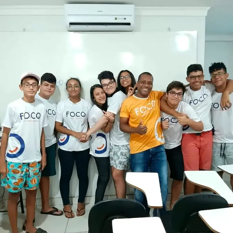 Turma do Foco de camisa branca do curso, abraçada e sorrindo diante do quadro branco